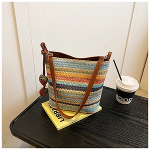 Detail of multi-color striped woven bucket bag with leather strap and strawberry charms