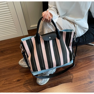 Detail of pink and black striped tote bag featuring black leather flap and round handles