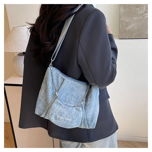 Detail view of light blue denim tote with metal chain and Happy Sunday pouch on model