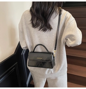 Detailed view of black PU leather handbag with gold buckle and embossed text