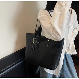 Detail of black tote bag with crocodile texture, metal rivets and a puppy charm