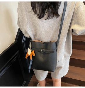 Detail of black lychee grain leather bucket bag with orange pegasus charm on model