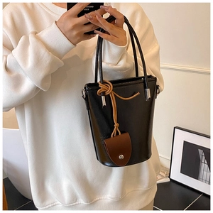 Minimalist black glossy bucket bag with brown leather charm and slim shoulder strap detail