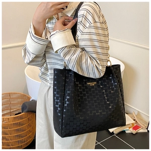 Détail du sac cabas noir avec lettrage embossé et plaque dorée porté à l'épaule pour femme