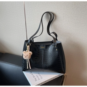 Detail of black crocodile pattern tote bag with teddy bear pendant and gold metal hardware