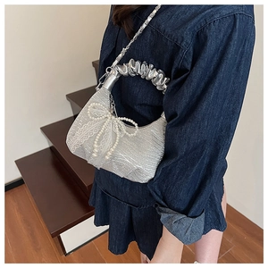 Detail of silver pleated handbag featuring a white lace bow and elegant pearl charms