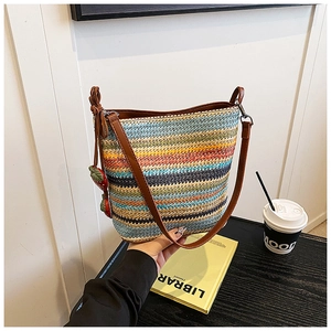 Close-up of rainbow striped woven bag with brown leather strap and strawberry charms