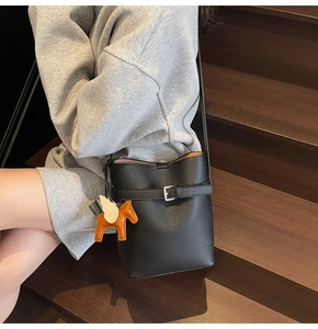 Detail of black lychee grain bucket bag featuring a Pegasus charm on wooden stairs