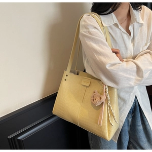 Detail of yellow crocodile pattern tote bag with teddy charm and stripe rope handle