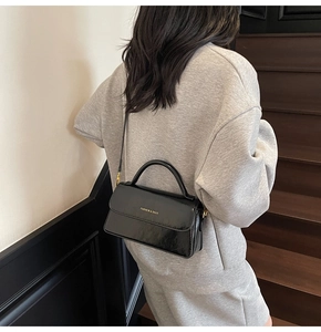 Model view showing the back of a vintage black glossy crossbody bag with metallic buckle