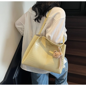 Detail of light yellow crocodile embossed tote bag with plush bear charm on a model