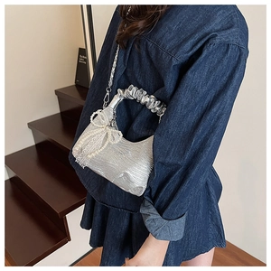 Detail of silver pleated handbag featuring lace bow, pearl charms and metal chain strap