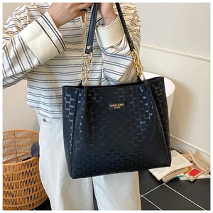Détail du sac en cuir gaufré noir avec bandoulière chaîne dorée et logo métallique