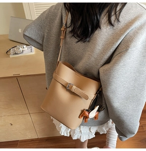 Detail of beige lychee pattern bucket bag with leather horse charm and adjustable strap