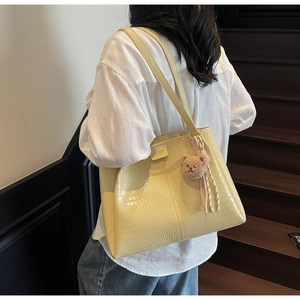 Detail of yellow crocodile pattern tote bag with shoulder straps and plush bear charm