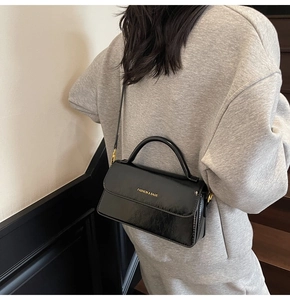 Detailed view of a black glossy crossbody bag worn by a model on a staircase