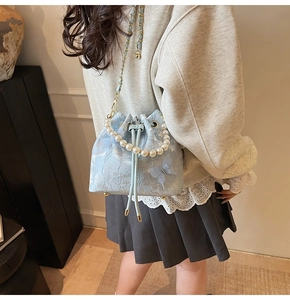 Close-up of light blue lace bucket bag with pearl handle on model's shoulder