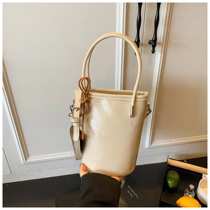 Detail view of cream white bucket bag featuring glossy crinkle texture and slim handle