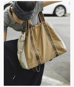 Detail of a large brown and beige tote bag featuring drawstring closure and striped handles