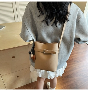 Close-up of khaki litchi grain bucket bag with a horse charm and thin shoulder strap