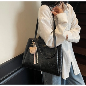Close-up of black crocodile texture tote bag with shoulder straps and plush bear charm