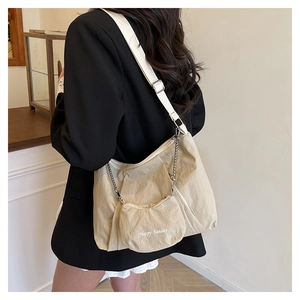 Detail of pleated beige tote bag with a Happy Sunday charm pouch on a black suit