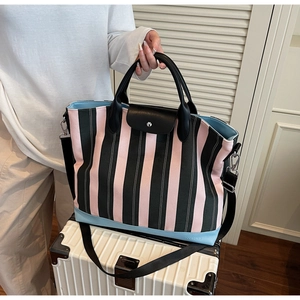 Detail of striped tote bag with leather trim and NOCO logo on a white suitcase