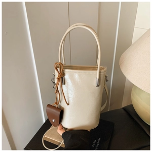 Close-up of cream-white bucket bag featuring smooth PU leather and mini brown charm