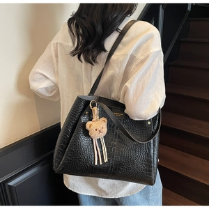 Close-up of black crocodile pattern tote bag with plush bear charm and long tassels