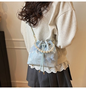 Close-up of light blue bucket bag with floral lace, pearl handle and 3D butterfly detail