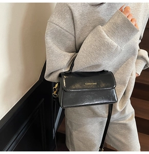 Close-up of black glossy leather crossbody bag with gold hardware and logo detail