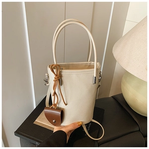 Detail of a creamy white bucket bag featuring fine leather texture and brown pendant charm