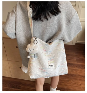 Close-up of white quilted tote bag with colorful embroidery and a cute cloud charm accessory