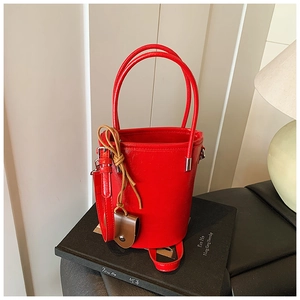 Detailed view of glossy red bucket bag with dual handles and detachable leather strap