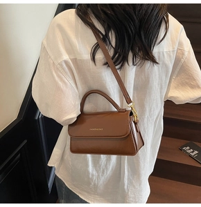 Brown leather handbag with gold lettering carried by a model on a white shirt