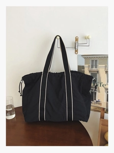 Detail of black large capacity tote bag with striped straps and drawstring side closure