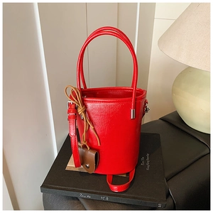 Close-up of a red bucket bag with polished faux leather texture on black books
