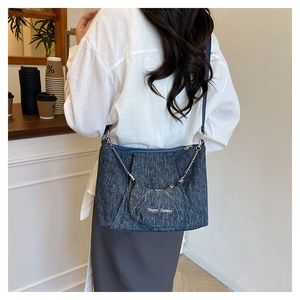 Detail of blue denim crescent bag with Happy Sunday embroidery and mini pouch attachment