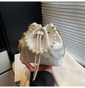 Close-up of white lace bucket bag featuring 3D butterfly decor and a large pearl handle