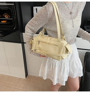Detail view of cream shoulder bag featuring zipper pockets and side metal buckle design
