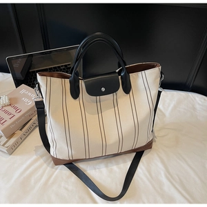 Detail of striped canvas tote bag with black leather handle and adjustable shoulder strap