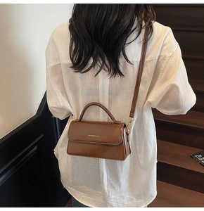 Detail view of a vintage brown crossbody bag with gold hardware on a white shirt