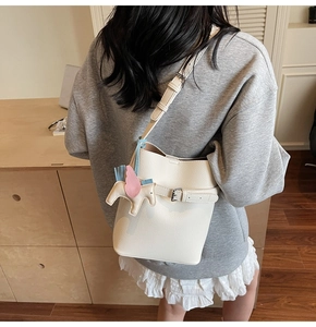 Detail view of cream lychee texture bucket bag featuring a cute unicorn bag charm
