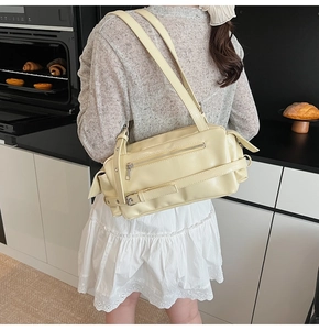 Detail of a creamy yellow pillow bag with a metal buckle and front zipper pocket