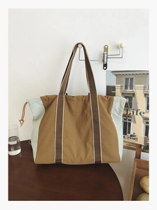 Detail of a large color-block tote bag with dual handles and side drawstring on wood