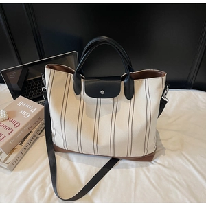 Detail of canvas tote bag with brown stripes and black leather flap on a white bed