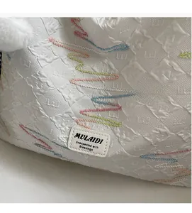 Detail of white quilted canvas tote with colorful wave embroidery and leather logo patch