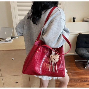 Close-up of red crocodile texture tote bag with plush bear charm and gold stud details