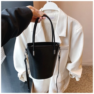 Detail of a minimalist black shiny leather bucket bag with silver metal handle connectors