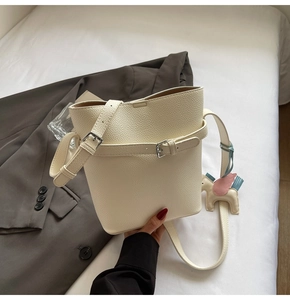 Detail of cream lychee leather bucket bag featuring a decorative Pegasus pendant and strap